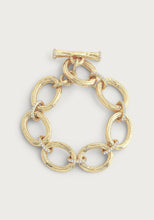 Load image into Gallery viewer, Introducing the Enchanted Forest Chain Bracelet, crafted with a gold-dipped brass chain featuring large, oval links seamlessly connected by smaller, textured rings. This bracelet is elegantly finished with a toggle clasp and includes delicate decorative details like hand-set crystals placed at intervals. Its shiny finish lends it an elegant and luxurious appearance when set against a plain background.
