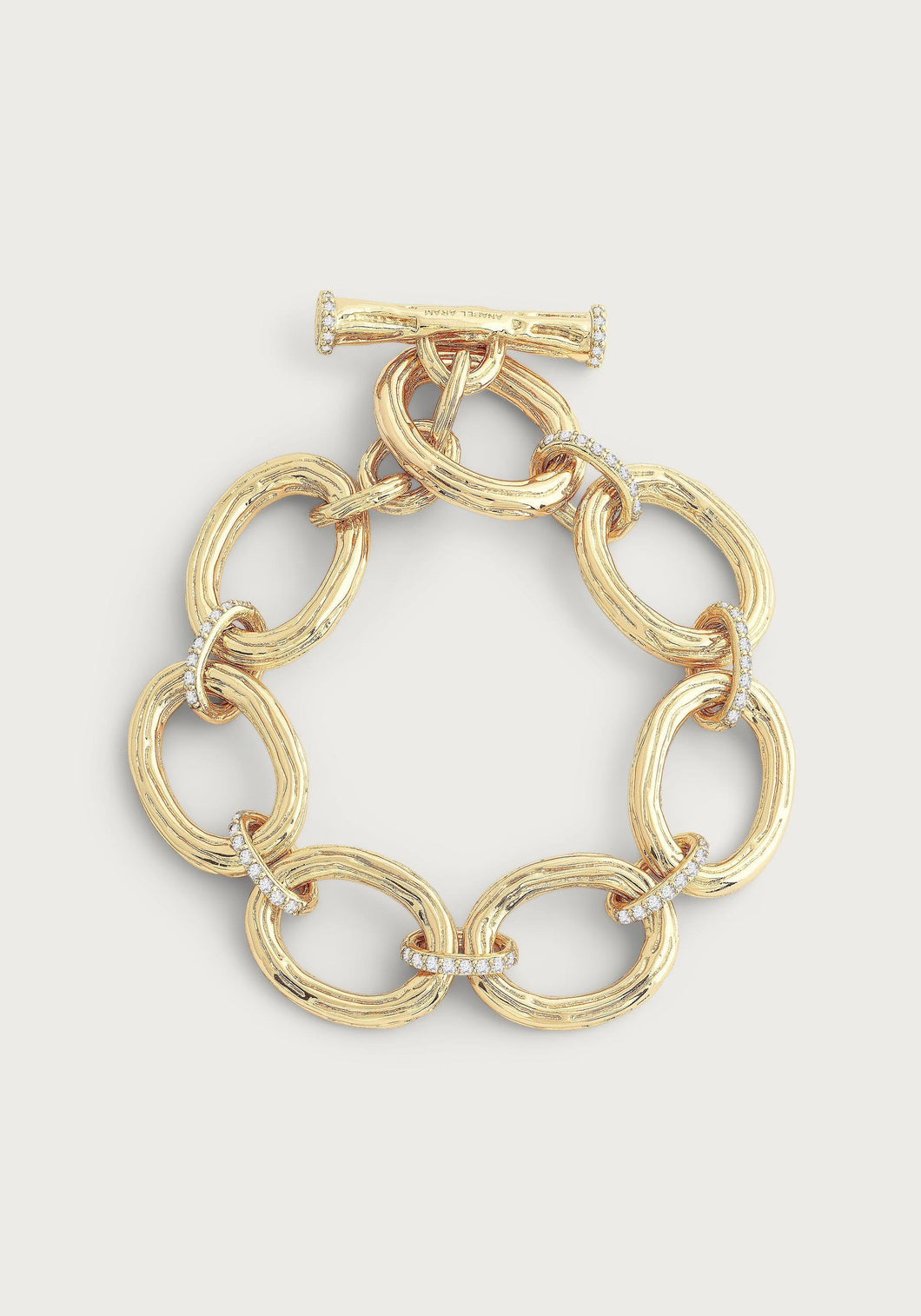 Introducing the Enchanted Forest Chain Bracelet, crafted with a gold-dipped brass chain featuring large, oval links seamlessly connected by smaller, textured rings. This bracelet is elegantly finished with a toggle clasp and includes delicate decorative details like hand-set crystals placed at intervals. Its shiny finish lends it an elegant and luxurious appearance when set against a plain background.