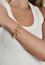 Load image into Gallery viewer, A person wearing a white ribbed tank top is spotlighting the stunning Enchanted Forest Chain Bracelet on their wrist, a chunky chain bracelet with large interlocking links crafted from gold-dipped brass. The individual&#39;s head and other hand are concealed, directing all attention to the captivating bracelet.
