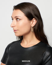 Load image into Gallery viewer, A person with long brown hair is wearing The Icon - Pave Hoop Earrings and a black leather top. They are looking to the left against a plain white background. Below the image, the word &quot;MEDIUM&quot; is visible in white text.
