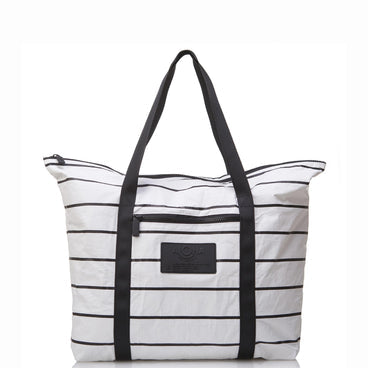 The Aloha Zipper Tote is a bestselling classic white duffle with horizontal black stripes, sturdy black handles, and a front zipper pocket with a black patch logo. Its spaciousness and simple, modern design make it perfect for travel or casual use.