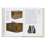The open book, titled *Little Book of Louis Vuitton*, presents vintage luggage in a luxury fashion. On the left page, it features two stacked Louis Vuitton trunks next to a suitcase embellished with leather and metal accents. The right page contains text and an image of a monogrammed bag with sophisticated white straps.