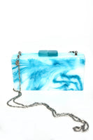 Load image into Gallery viewer, The Large Resin Clutch, featuring a marbled turquoise and white rectangular design, includes a shiny silver chain strap and a turquoise clasp. Its colors and texture are accentuated against a plain white background, creating an artistic wardrobe piece.
