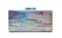 Load image into Gallery viewer, The Large Resin Clutch is a sleek, rectangular purse with a smooth marbled design in blue, purple, and cream shades. Its small clasp matches these colors, enhancing its artistic appeal. A white background accentuates the vibrant hues beautifully.
