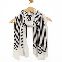 Load image into Gallery viewer, A white Lightweight Patterned Scarf with black geometric stripes draped over a wooden hanger features abstract splashes and zigzag edges. Made of lightweight material for warmth, it offers dynamic style against a plain white backdrop for a minimalist look.
