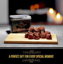Load image into Gallery viewer, A tin of Cocoa Dusted Truffles rests on a wooden board with sea salt truffles. Soft bokeh lights in the background add warmth. The text reads: &quot;A Luxurious Gift For Every Special Moment.
