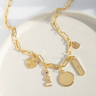 Load image into Gallery viewer, The Multi-Charm Link Necklace, gold-plated with various pendants, rests on a white surface. It features a circular plate, rectangular tag, abstract face with an eye, coin-like charm, textured round disc, and elegant elongated rectangular links.
