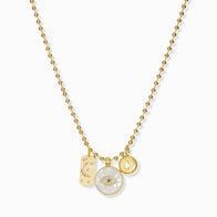 Load image into Gallery viewer, The Ball Chain Charm Necklace features a gold chain adorned with a small engraved rectangular tag, a circular pendant with a blue gem eye, and an elegant mother of pearl tile disc. Its simple design stands out beautifully against the white background.
