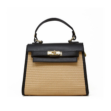 Load image into Gallery viewer, The Raffia Leather Bag features a trapezoidal design with a black Italian leather top flap and handle. Its body is crafted from textured beige material resembling woven straw, adorned with a gold-tone clasp closure on the flap and an adjustable handle for added versatility.
