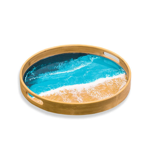 This round bamboo serving tray is a perfect addition to any Ocean trays collection, featuring an artistic resin inlay of blue waves and sandy shore. Two oval handholds make it easy to carry.