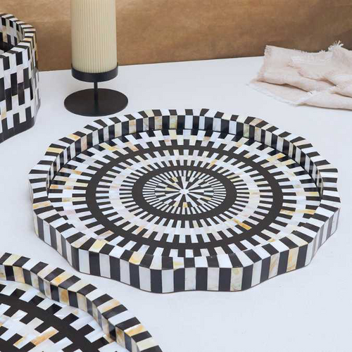 The Finlay Inlay Tray, handcrafted in India with a black and white geometric pattern of alternating rectangular inlays, sits on a white surface. A black candlestick and folded beige cloth are visible in the background.