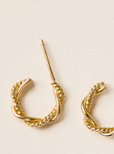 Load image into Gallery viewer, A close-up of a 14k gold-filled Braided Mini Hoop earring, featuring a rope-like texture, rests on a flat, off-white surface. The earring&#39;s post extends upwards while another matching piece is partially visible, indicating it&#39;s part of the Braided Mini Hoops pair. The lighting accentuates the shiny and intricate detailing of these everyday earrings.
