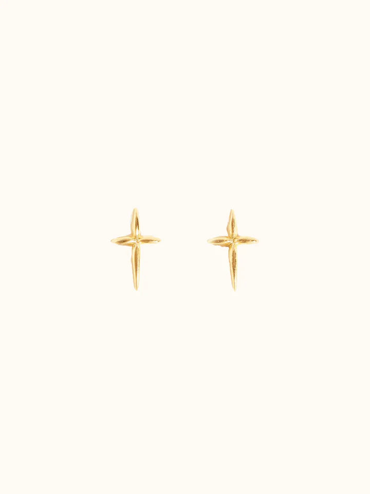 A pair of Droplet Cross Studs, minimalist vermeil stud earrings shaped as small, angular crosses on a plain off-white background. Handmade in Nashville, they feature a polished finish that exudes a subtle shine. The studs are symmetrically positioned to showcase their intricate detailing.