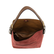 Load image into Gallery viewer, The Hobo 2 in 1 Faux Suede Handbag is a vegan leather accessory in brown and red, showcasing an open top that reveals an interior lined with lighter brown fabric. It includes a single handle and a removable crossbody strap for versatility, secured with a snap button closure. Inside, you&#39;ll find a zippered pocket for added convenience. The exterior boasts a smooth texture and features an additional front pocket.
