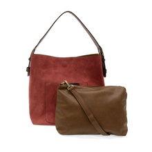 Load image into Gallery viewer, The Hobo 2 in 1 Faux Suede Handbag features a red faux suede tote bag with a brown leather handle and front pocket, beautifully complemented by a smaller vegan leather crossbody bag. Both bags are adorned with gold-tone hardware, and the crossbody includes an adjustable, removable strap. This stylish duo is set against a plain white background.
