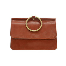 Load image into Gallery viewer, Introducing the Aria Ring Bag - Fall/Winter: a vegan leather clutch in a sophisticated brown hue, complete with a chic flap design. Its standout feature is a large gold metallic ring at the top center, adding both style and functionality by serving as an eye-catching handle or wearable bracelet bag. The clutch&#39;s smooth texture is beautifully highlighted against a plain white background.
