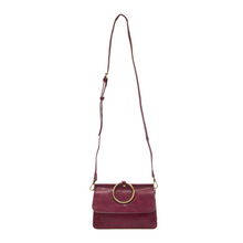 Load image into Gallery viewer, Introducing the Aria Ring Bag - Fall/Winter: a chic crossbody bracelet bag in vibrant red, expertly fashioned from vegan leather. It features a refined flap closure with an elegant gold circular buckle and comes with an adjustable, detachable shoulder strap adorned with gold hardware. The bag&#39;s sleek, minimalist design is enhanced by its subtly glossy finish.
