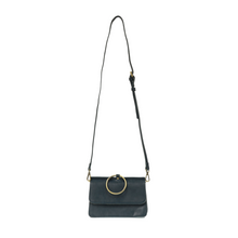 Load image into Gallery viewer, The Aria Ring Bag - Fall/Winter is a black vegan leather crossbody bag featuring a detachable shoulder strap. It boasts a flap closure adorned with a prominent circular gold ring accent on the front. Its minimalist design exudes elegance, making it perfect for both casual and formal occasions.
