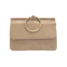 Load image into Gallery viewer, Introducing the Aria Ring Bag - Fall/Winter edition, a beige vegan leather clutch designed with a sleek flap and accented by a prominent gold ring handle at the top center. This clutch boasts a smooth texture with subtle edge stitching, exuding an elegant minimalist style. For ultimate versatility and sophistication, it features a detachable shoulder strap to enhance its functionality as a bracelet bag.
