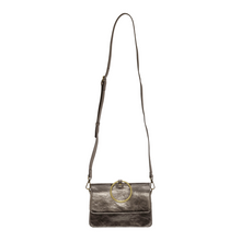 Load image into Gallery viewer, The Aria Ring Bag - Fall/Winter, crafted from vegan leather in a striking metallic bronze, includes a long, adjustable and detachable shoulder strap. It showcases a front flap adorned with a prominent circular brass accent. The bag&#39;s sleek and shiny finish complements its elegant design, making it ideal for both casual and formal settings.
