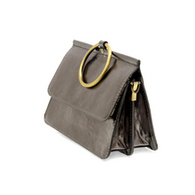 Load image into Gallery viewer, Introducing the Aria Ring Bag - Fall/Winter, a chic accessory crafted in metallic gray vegan leather. Its structured, trapezoidal shape exudes elegance with a shiny finish that reflects light beautifully. This stylish bracelet bag features a standout large circular gold handle and a sophisticated flap closure. Additionally, it includes a gold side zipper for an extra touch of sophistication.
