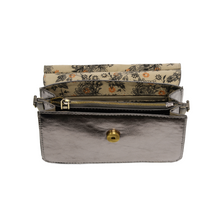 Load image into Gallery viewer, The Aria Ring Bag - Fall/Winter edition is displayed open, showcasing its interior. It features a luxurious floral pattern lining in black and orange hues. Crafted from vegan leather, this metallic silver clutch with a brass button clasp includes a gold zipper pocket and offers the option to attach a crossbody strap for added stylish convenience.
