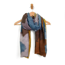 Load image into Gallery viewer, A Midweight Patterned Scarf with an abstract floral design is draped on a wooden hanger. It showcases a harmonious blend of multicolored hues, including blue, brown, gray, and mustard yellow. The fabric looks soft and lightweight, perfect for accentuating an outfit with vibrant colors.
