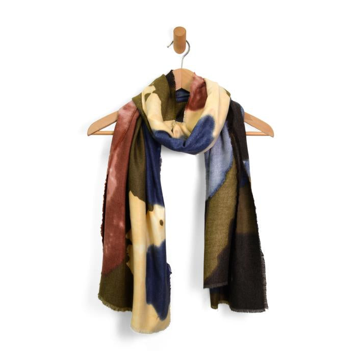 A Midweight Patterned Scarf, adorned with abstract floral designs in dark blue, olive green, beige, and maroon, elegantly drapes from a wooden hanger featuring a simple beige hook. With its soft fringed edges, the scarf exudes a cozy yet stylish charm. The plain white background accentuates the scarf's vibrant colors and rich texture.