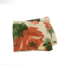 Load image into Gallery viewer, The Midweight Patterned Scarf, featuring oversized red and green floral designs on a cream backdrop, exudes elegance. Its lightweight, slightly sheer fabric drapes beautifully on a plain white surface, highlighting its delicate charm.
