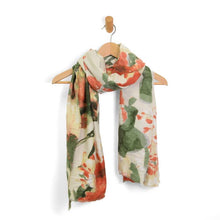 Load image into Gallery viewer, A chic Midweight Patterned Scarf featuring a blend of red, orange, and green hues gracefully hangs on a wooden hanger. The scarf sports an abstract floral design on a cream background, with slightly frayed ends adding a casual touch, elegantly displayed on a simple wall hook.
