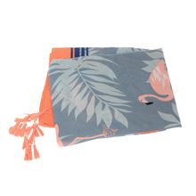 Load image into Gallery viewer, A Lightweight Patterned Scarf showcases a tropical design featuring pink flamingos and light blue palm leaves on a grey background, reminiscent of a folded beach towel. The scarf is accented with bright orange edges and coral tassels on one end.
