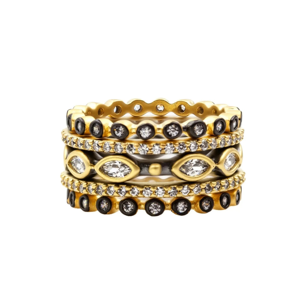 The Signature Marquise Station Ring Stack exudes captivating elegance with its set of four intricately designed gold rings. Two rings are adorned with round black stones, one showcases a marquise pattern enriched by clear stones and small diamonds, while the last features evenly spaced diamonds. These stackable rings vary in thickness and pattern, creating an ornate appearance.