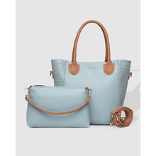 Load image into Gallery viewer, On display is a chic set of two handbags in light blue, made from vegan leather. The larger item, known as the Dublin Tote Bag, features brown handles and side accents. The smaller crossbody bag comes with a coordinating adjustable strap. Both bags present a sleek and modern design with understated branding on the front.
