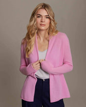 Load image into Gallery viewer, A person with long, wavy blonde hair is wearing a Cashmere Shrunken Duster in light pink over a white top and navy pants. They stand against a neutral gray background, looking directly at the camera with a calm expression, gently holding the soft Mongolian cashmere.
