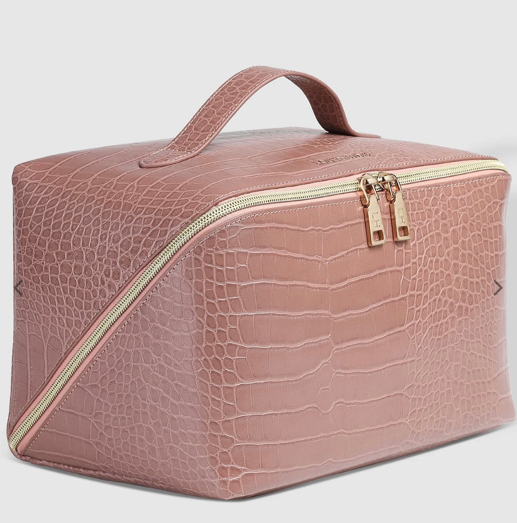 The Coordinating Toiletry and Makeup Case, crafted from pink faux crocodile leather, boasts a gold zipper with two pulls for easy access. Its top handle ensures convenient carrying, while it rests against a plain white background to emphasize its textured surface and structured design—ideal for organizing your essentials.