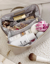 Load image into Gallery viewer, The Coordinating Toiletry and Makeup Cases in beige feature a textured faux croc finish, revealing two compartments lined with black and white stripes. Inside, you can see cosmetics, scrunchies, and a patterned hair tie. In the foreground on a white surface lies a makeup brush accompanied by a glass hair clip.
