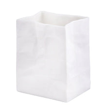 Load image into Gallery viewer, The Porcelain “Paper Bag” Vase is a white, bag-shaped vessel that stands upright, exuding an artisanal touch. Its surface is adorned with gentle creases and folds that mimic a real paper bag. This handcrafted porcelain piece features a rectangular base and a slightly uneven open top, making it a distinctive vase for any setting.
