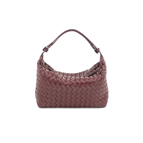 A Woven Handbag crafted from vegan leather is featured against a plain white backdrop. The handbag boasts a textured design with a complex interlaced pattern and is presented in deep burgundy. Its rounded handle enhances the bag's sophisticated appearance.