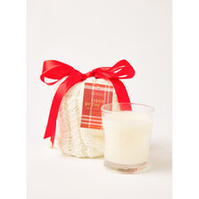 Load image into Gallery viewer, The Holiday Stocking Candle, infused with Sea Pines scent, is elegantly placed in a clear glass next to a knitted white pouch adorned with a red ribbon. The pouch features the festive label &quot;BEFORE BE IDER BY THE&quot; in white and red, creating a perfect holiday candle display against the simple white background.
