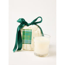 Load image into Gallery viewer, A Holiday Stocking Candle in a clear glass is placed next to a white knitted pouch, which is tied with a dark green ribbon. A checkered tag on the pouch displays &quot;Sea Pine&quot; in green and white, enhancing the cozy, festive ambiance with its Sea Pines Scent.
