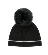 Load image into Gallery viewer, This Knit Beanie, adorned with a Crystal Contrast Line, features a black design with a large, fluffy fox fur pom-pom on top and boasts a ribbed texture with a white stripe near the base.
