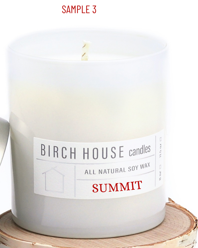 The Summit Candle, part of Birch House Candles, is a handmade white candle with an Amber Oak scent. Made from all-natural soy wax, it features a single wick and rests on a wooden slice. The label includes 