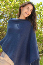 Load image into Gallery viewer, A woman with long brown hair smiles while wearing a Cashmere Poncho. She stands outdoors, surrounded by lush green foliage with sunlight filtering through the leaves, casting a warm glow. Her relaxed and happy expression radiates joy as she gazes slightly to the side.
