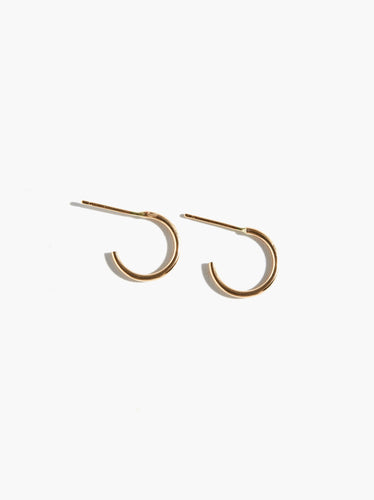 The Celine Huggie Hoops are showcased against a plain white background, highlighting their minimalist design. Made from 14k gold-filled material, these small and thin circular hoops offer a simple yet elegant look, ideal for everyday wear. They represent the brand's dedication to ethical fashion and sustainability.