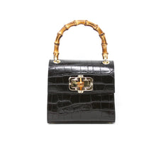 Load image into Gallery viewer, The Leather Bag With Bamboo Handle boasts a glossy black crocodile-textured Italian leather exterior, a bamboo handle, and a gold-detailed front clasp. Set against a white background, it highlights its structured elegance.
