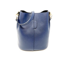 Load image into Gallery viewer, The Leather Bucket Bag is made from fine Italian leather with a textured blue surface. It includes a small handle, an adjustable shoulder strap with gold hardware, and its minimalist design shines elegantly against a plain white background.
