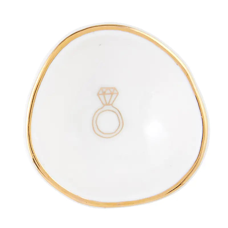 The Ring Dish is a small, elegant white ceramic bowl with an asymmetrical shape and gold-accented rim. It showcases a minimalist design with a simple gold outline of a diamond ring at the center, perfect for stylishly storing your rings. Ideal for those who value refined style in ceramics.