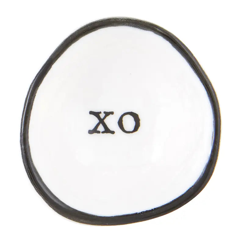 The Ring Dish is a small, irregularly shaped white ceramic piece with a smooth texture, featuring a thin black border and bold "XO" text at the center—ideal for storing your rings.