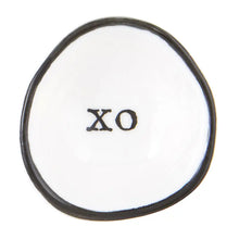 Load image into Gallery viewer, The Ring Dish is a small, irregularly shaped white ceramic piece with a smooth texture, featuring a thin black border and bold &quot;XO&quot; text at the center—ideal for storing your rings.
