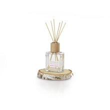 Load image into Gallery viewer, A minimalist square glass bottle with a wooden cap holds reed sticks, infused with essential oils for the Sweet Grapefruit Diffuser fragrance. This &quot;Birch Bliss&quot; scent hints at sweet grapefruit and sits on a circular birch wood slice against a plain white backdrop.
